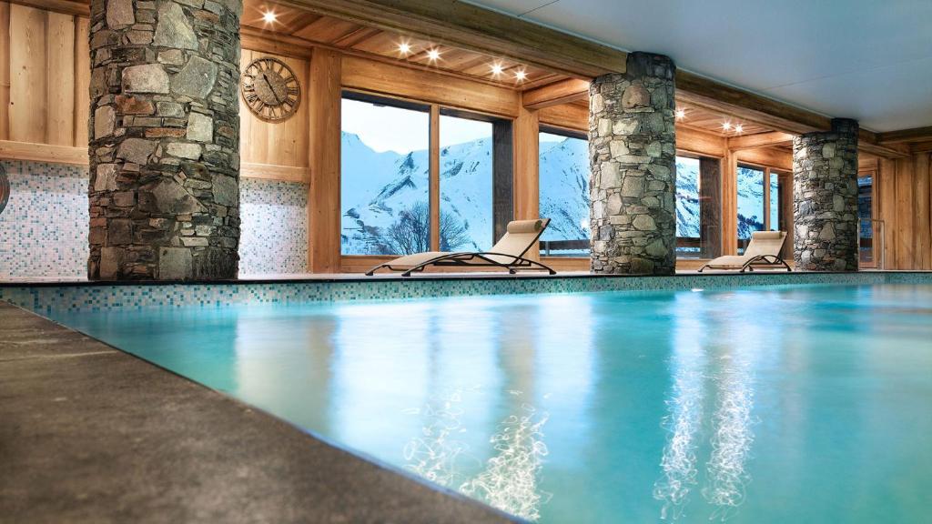 a swimming pool with chairs in a room with mountains at Les Chalets Du Gypse in Saint-Martin-de-Belleville