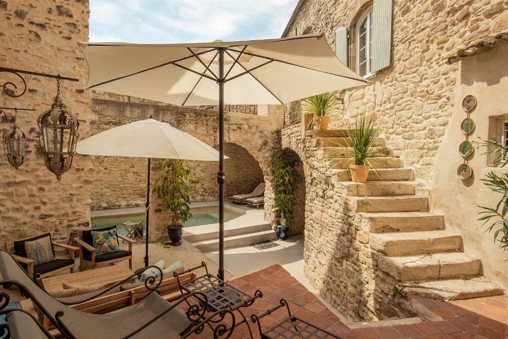 a patio with an umbrella and chairs and a pool at LA FUGUE chambres d' hôtes de charme , DEMEURE HISTORIQUE,PISCINE,JARDIN proche UZES NIMES ALES in Brignon