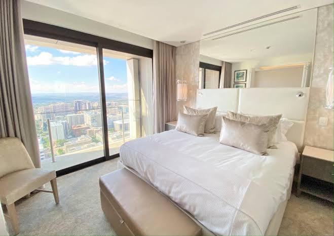 Cama blanca grande en habitación con ventana grande en Sandton Skye Exclusive Apartment, en Johannesburgo