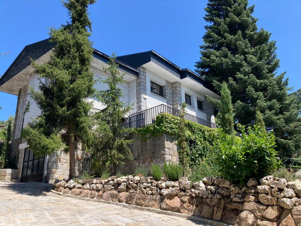 una casa con una pared de piedra y árboles en Gran chalet con piscina y apartamento en Navacerrada en Navacerrada