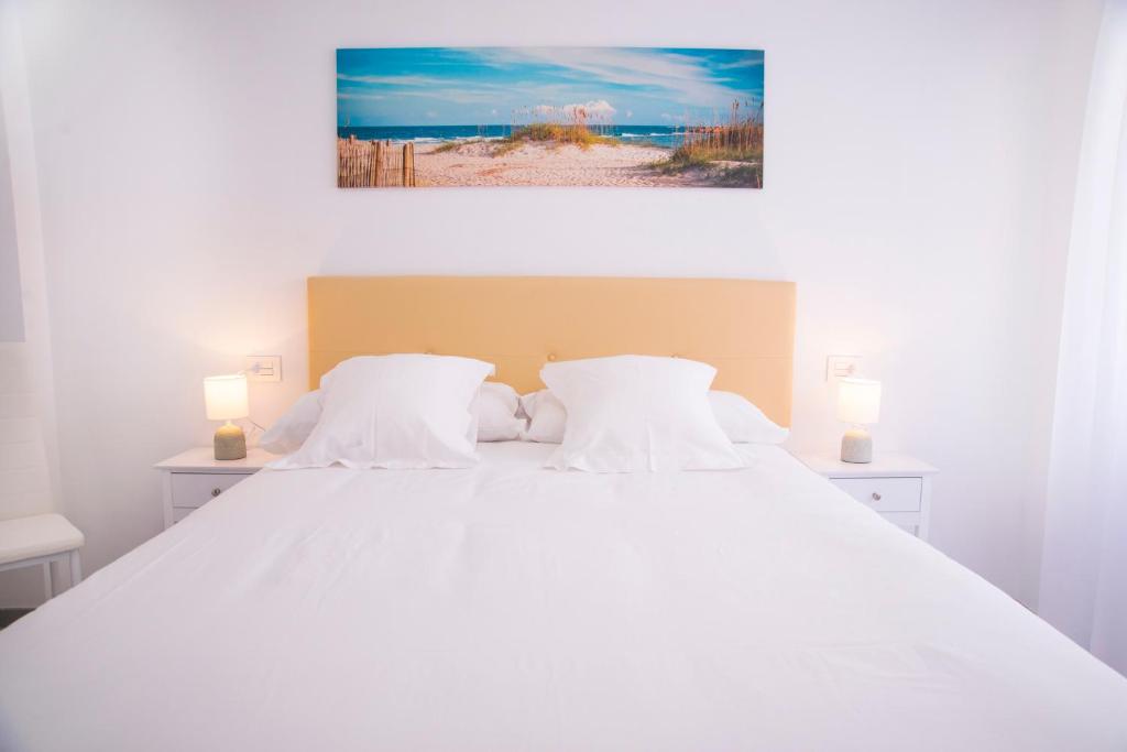 a white bed with white pillows and a painting on the wall at O Grove Centro con vistas a La Toja parking in O Grove