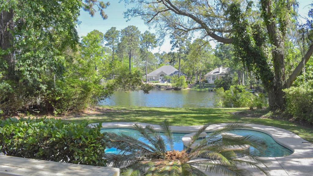 a swimming pool in front of a lake with trees at 20 Port Tack in Hilton Head Island