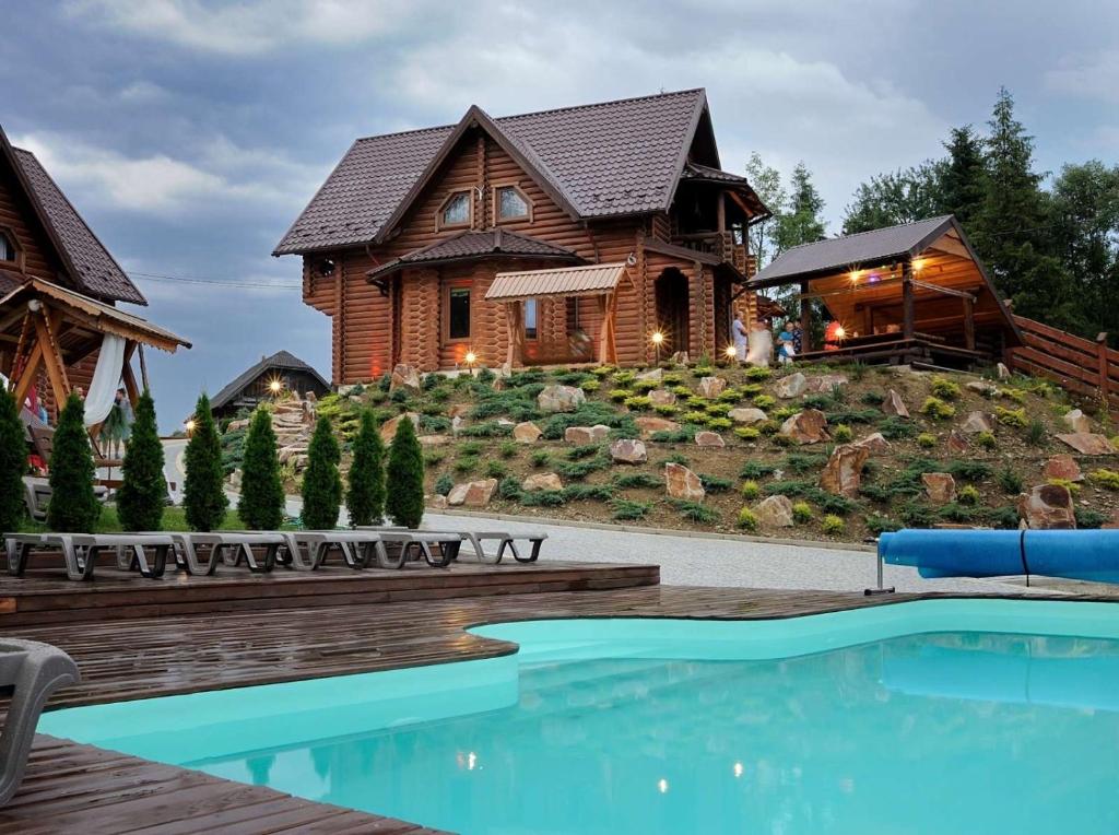 une maison en rondins avec une piscine en face de celle-ci dans l'établissement Смарагдовий пагорб, à Plavie