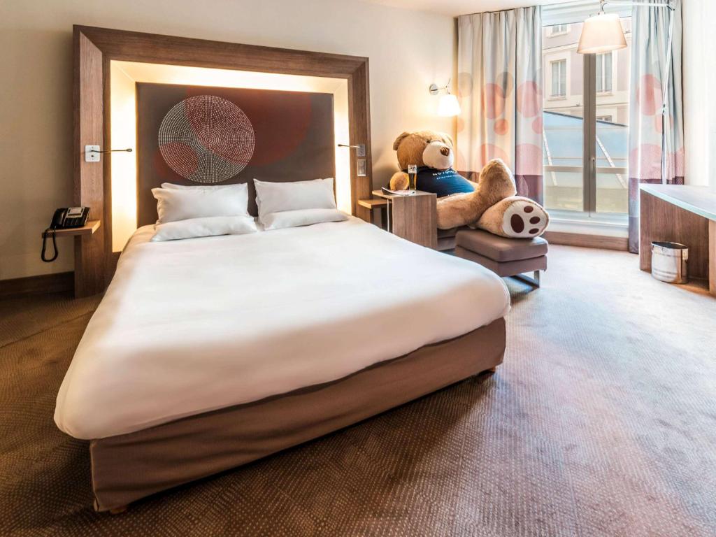 a large bed with a teddy bear sitting in a chair at Novotel Toulouse Centre Wilson in Toulouse