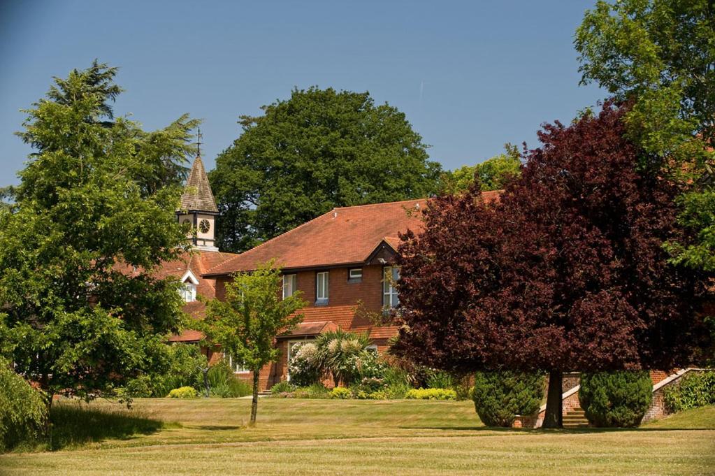 a large brick house with a church in the background at Roffey Park Venue in Horsham