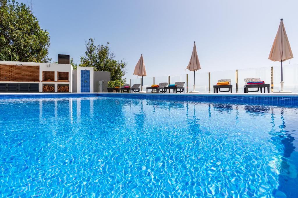 a blue swimming pool with chairs and umbrellas at SUNNYSIDE VILLA in Calheta