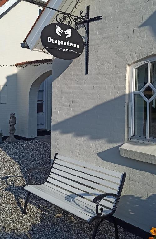 a white bench in front of a building with a sign at Dragondrum Bed & Kitchen in Ullerslev