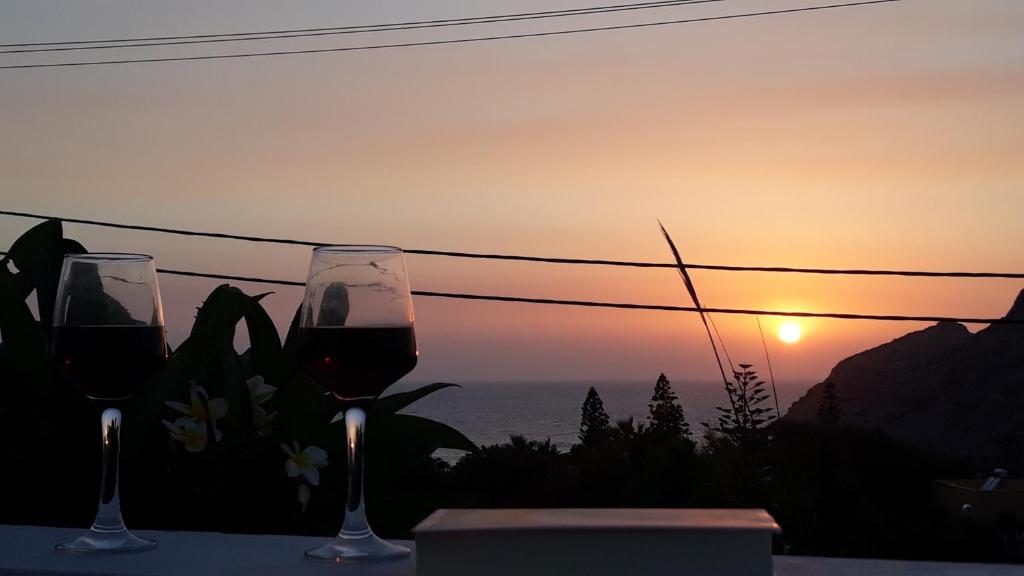 two glasses of wine sitting on a table with the sunset at Sunset Suites 'Annada in Arkasa