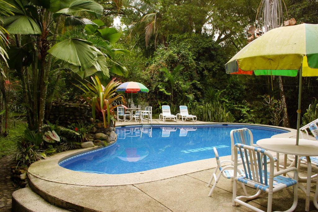 a swimming pool with chairs and tables and an umbrella at Cabinas Iguana Cahuita in Cahuita
