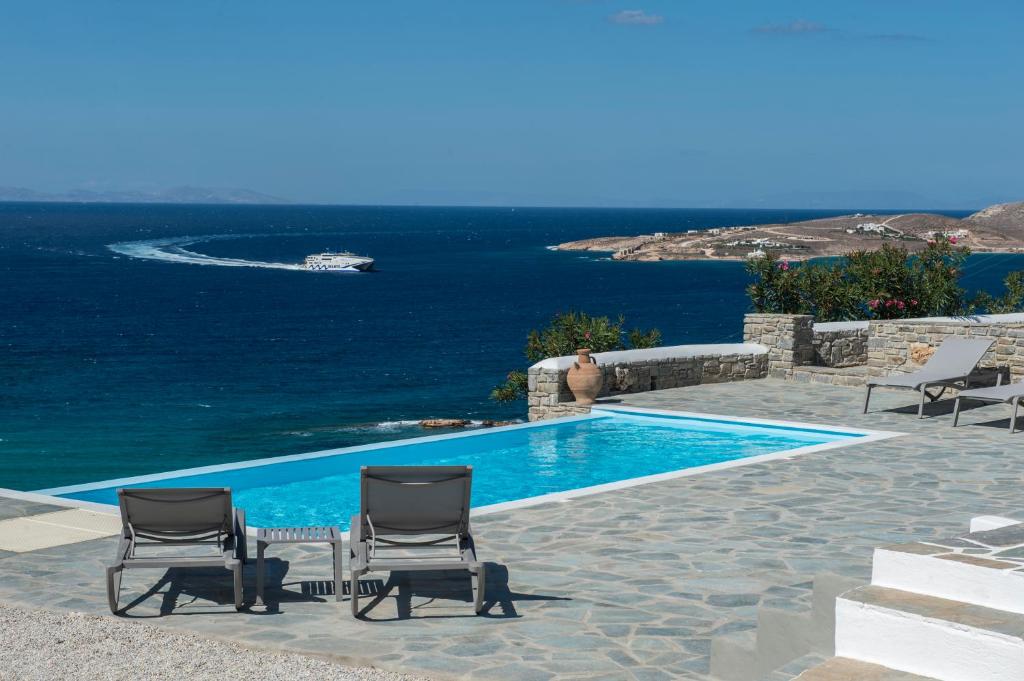 a swimming pool with two chairs and the ocean at Anemos in Parikia
