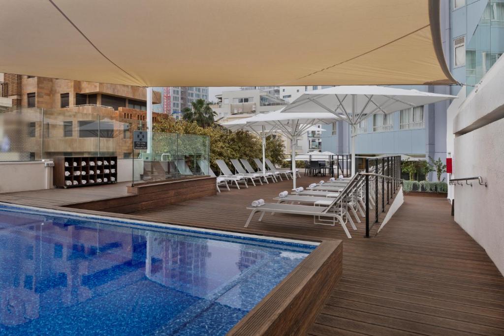 an outdoor swimming pool with chairs and umbrellas on a building at Metropolitan Hotel in Tel Aviv