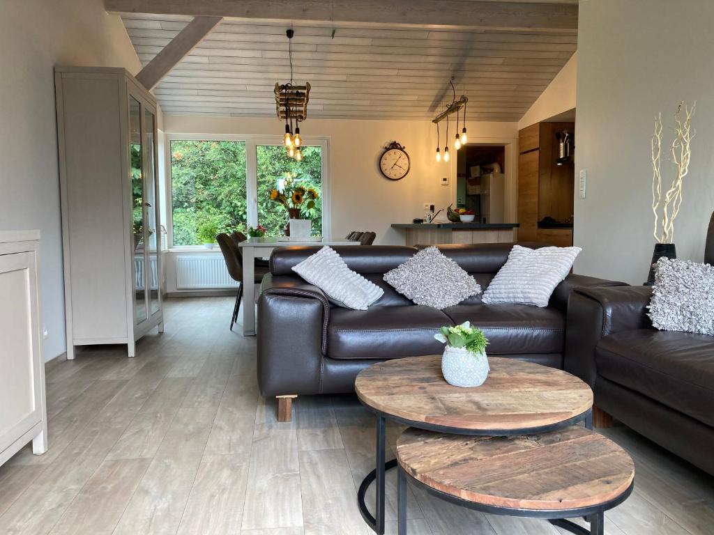 uma sala de estar com um sofá de couro e mesas em Chalet des Campanules avec Sauna em Vielsalm