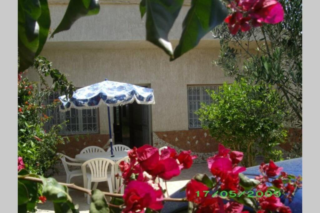 a patio with chairs and an umbrella and pink flowers at Petite Villa à Sidi Rahal Plage in Sidi Rahal