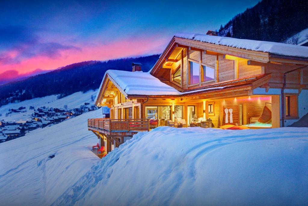 a house in the snow with the sun setting at Chalet Alti - OVO Network in Le Grand-Bornand