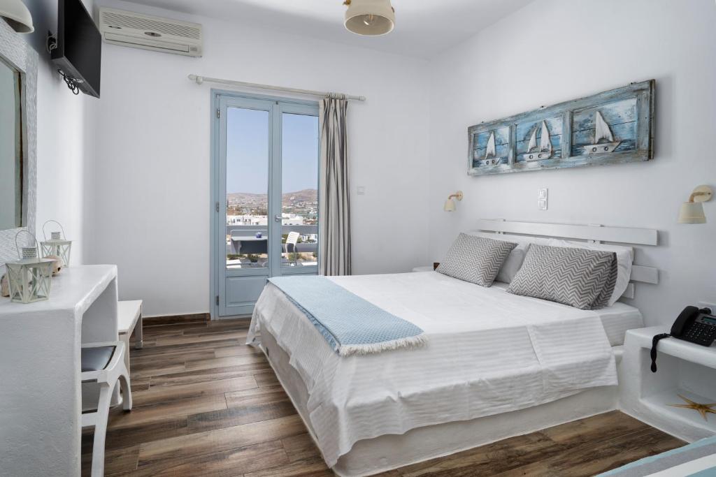a white bedroom with a bed and a large window at Hotel Iris in Naousa