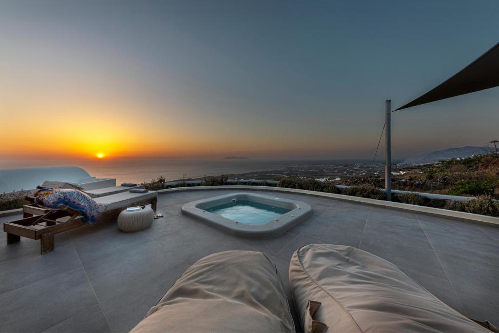 een hot tub op een patio met de zonsondergang op de achtergrond bij Villa Vinea Santorini in Imerovígli