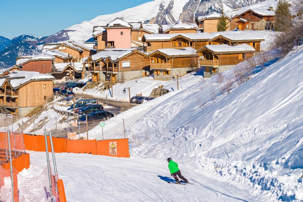 a person skiing down a snow covered slope in front of a resort at travelski home select - Chalets Le Grand Panorama II 3 stars in Valmeinier