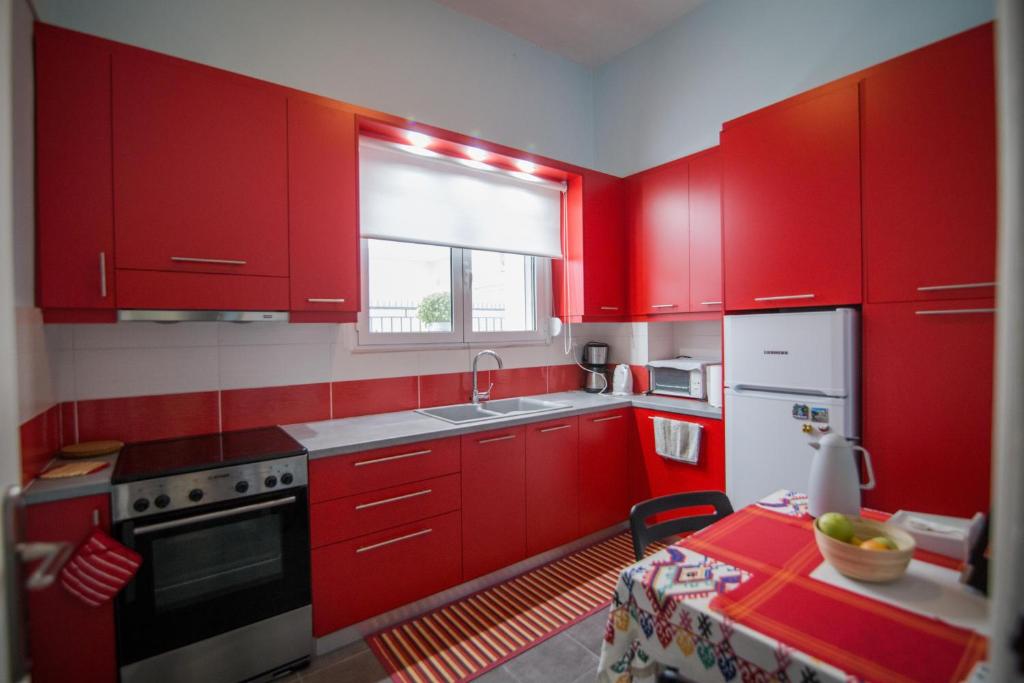 a kitchen with red cabinets and a table and a window at ΑΝΑΚΑΙΝΙΣΜΕΝΗ ΜΟΝΟΚΑΤΟΙΚΙΑ 125 τμ ΣΤΟ ΚΕΝΤΡΟ ΜΕ ΚΗΠΟ in Missolonghi