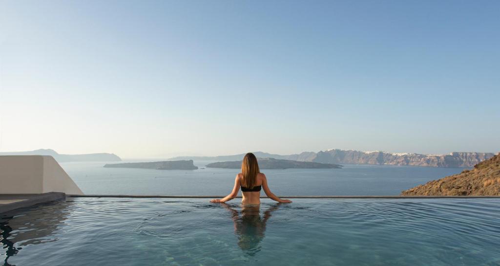 una mujer sentada en una piscina infinita con vistas al agua en Santonero - The Philoxenia Project, en Akrotiri