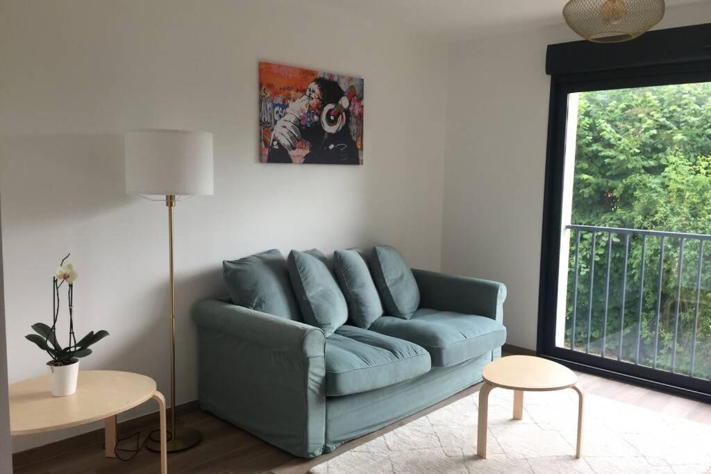 - un canapé bleu dans le salon doté d'une fenêtre dans l'établissement Superbe appartement avec vue sur la tour Eiffel, à Saint-Leu-la-Forêt