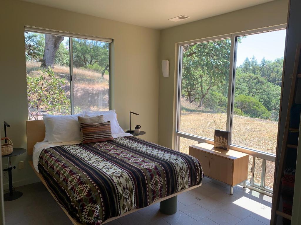 a bedroom with a bed and two large windows at DogWood Cottage in Ukiah