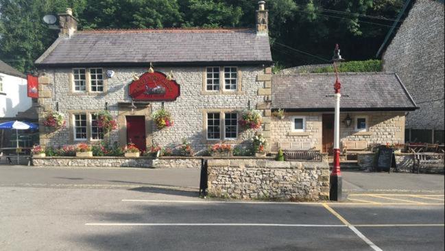 a stone building with a red sign in a parking lot at Anglers rest in Millers Dale