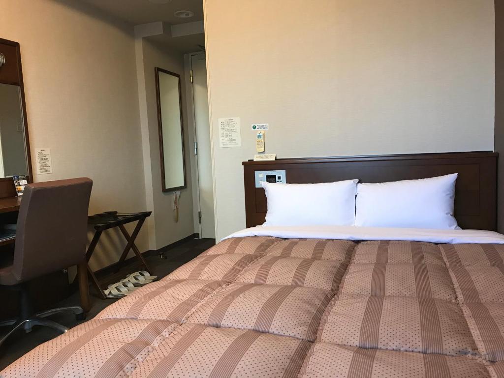 a bedroom with a bed with white pillows and a desk at Hotel Route-Inn Sendainagamachi Inter in Sendai