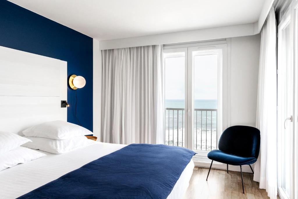 a bedroom with a bed and a chair and a window at Hôtel Le Windsor Biarritz in Biarritz