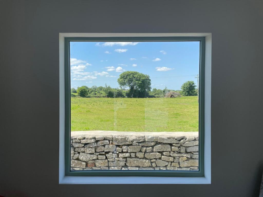 una ventana con vistas a una pared de piedra y a un campo en The Potters Lodge, en Carrick on Shannon