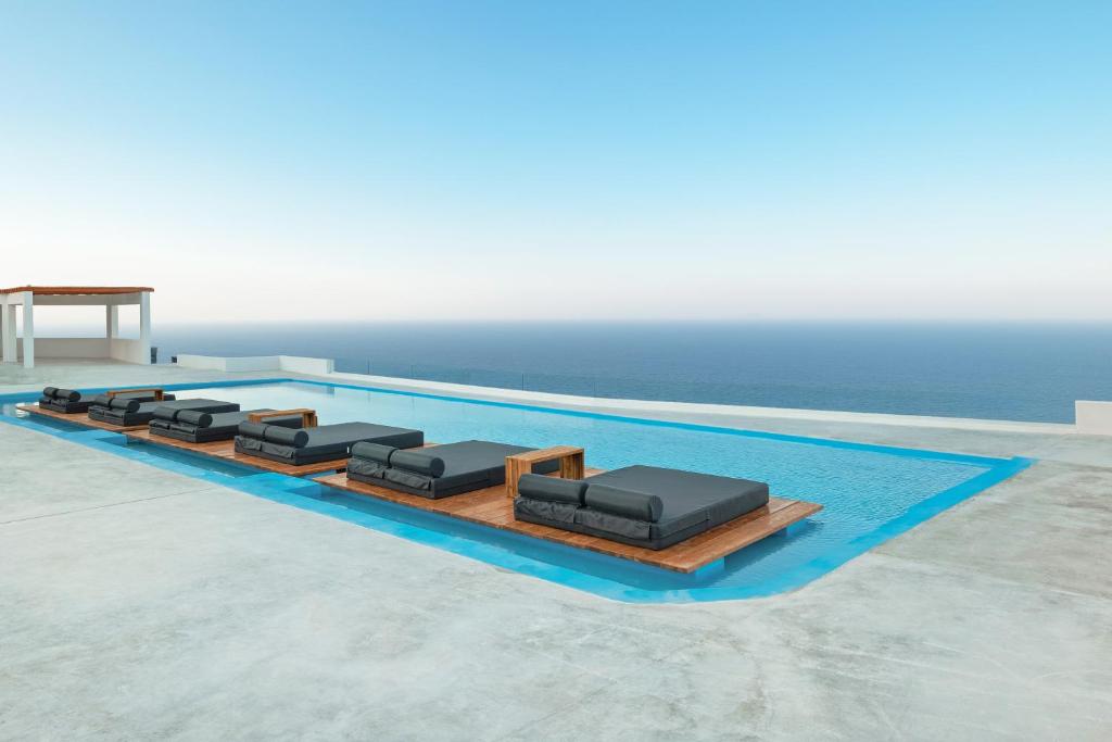a pool with four chaise lounges next to the ocean at Oyster Luxury Suites in Imerovigli