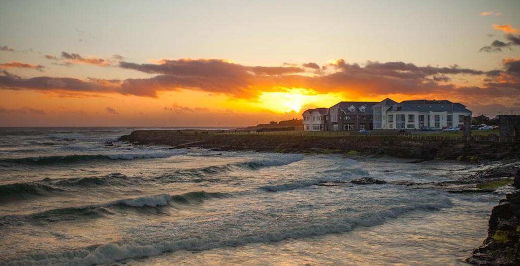 una puesta de sol sobre una playa con casas y el océano en Armada Hotel, en Spanish Point