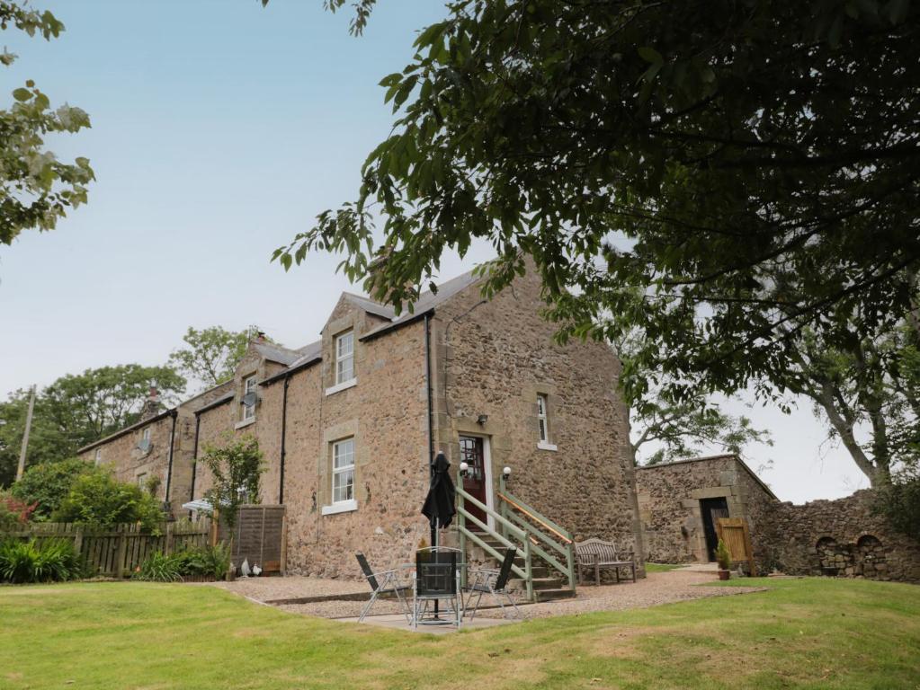 un antiguo edificio de ladrillo con una escalera delante de él en 1 Roddam Rigg Cottage, en Alnwick