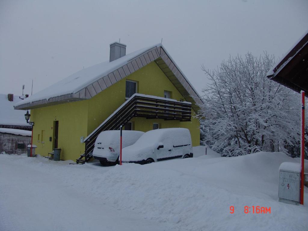 uma casa amarela com carros cobertos de neve estacionados em frente em Apartmány u Torína em Boží Dar