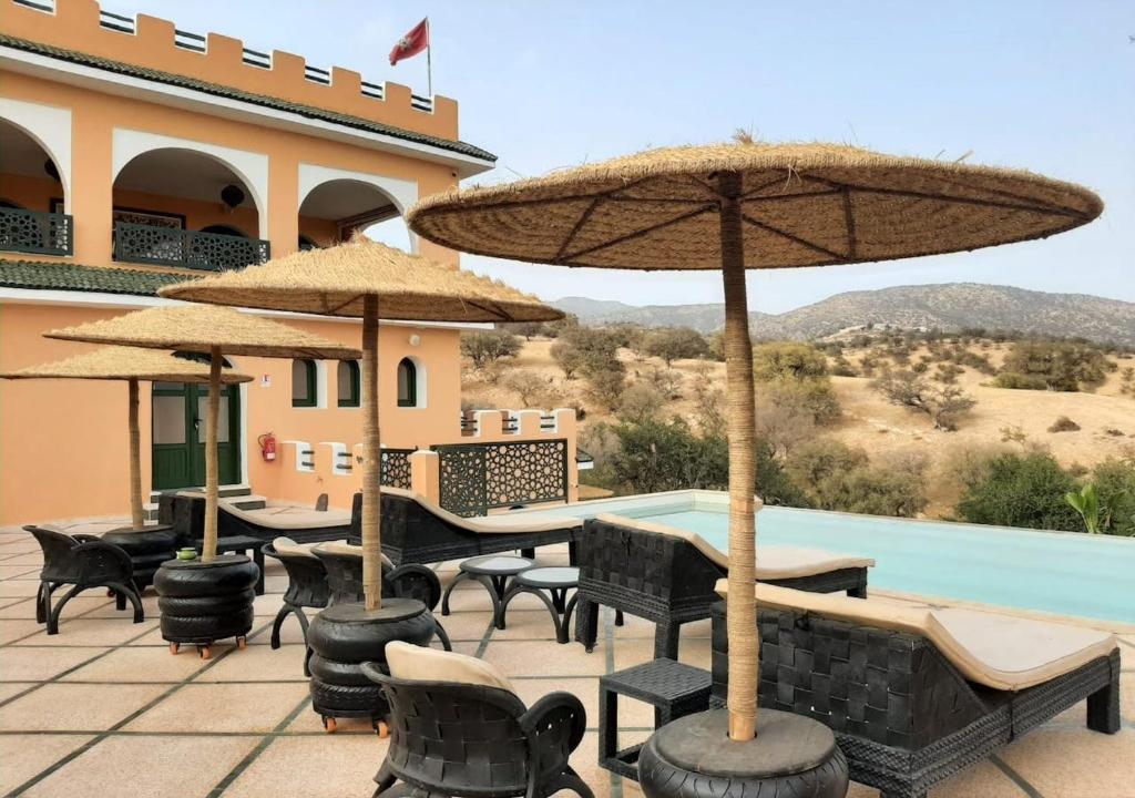 eine Terrasse mit Tischen, Stühlen und Sonnenschirmen neben einem Pool in der Unterkunft Gîte Forest Kasbah in Kasba et Tahar