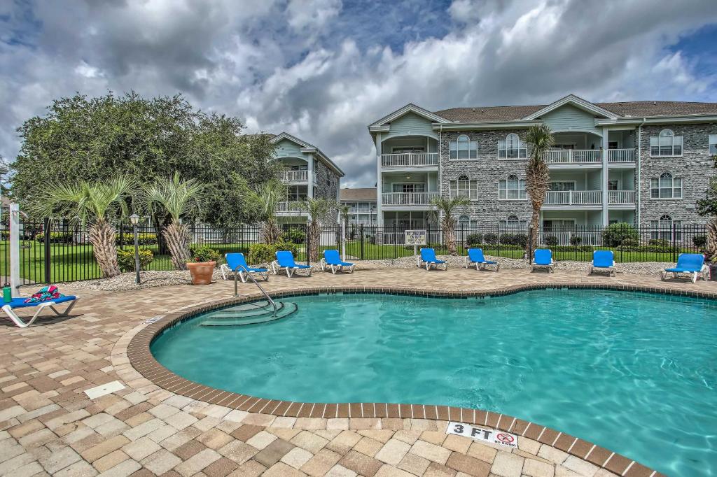 a swimming pool with blue chairs and a building at Lovely Myrtle Beach Condo 4 Mi to Boardwalk! in Myrtle Beach