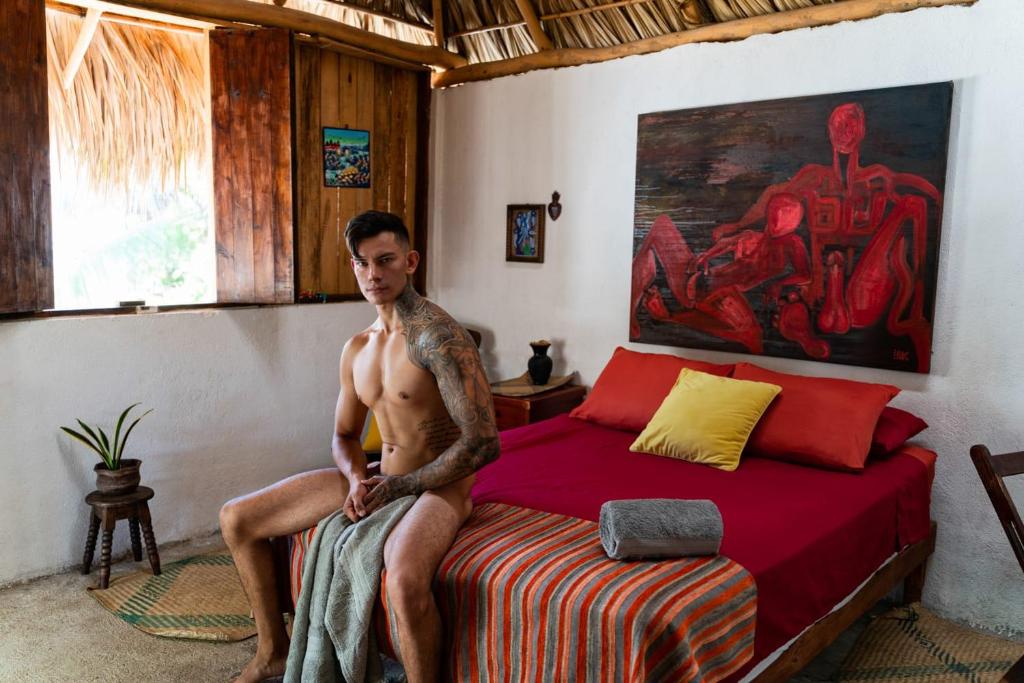 a man with a tattoo sitting on a bed at La Máxima Drag Show & Bar LGBT in Zipolite