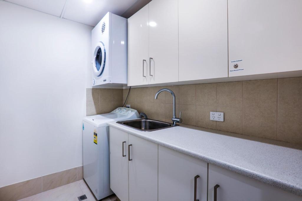 a kitchen with white cabinets and a sink and a dishwasher at The Breakers in Gold Coast