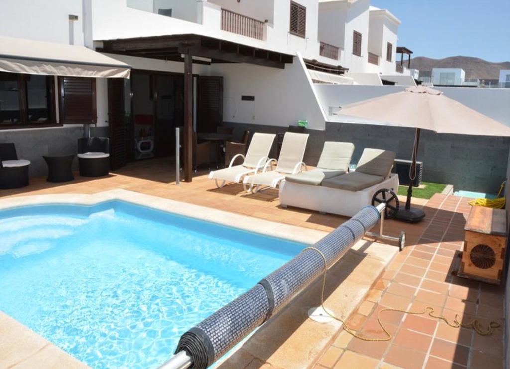 a swimming pool with an umbrella and chairs on a building at Beautiful and luxurious villa with heated pool and free Wi-Fi in Playa Blanca. in Playa Blanca