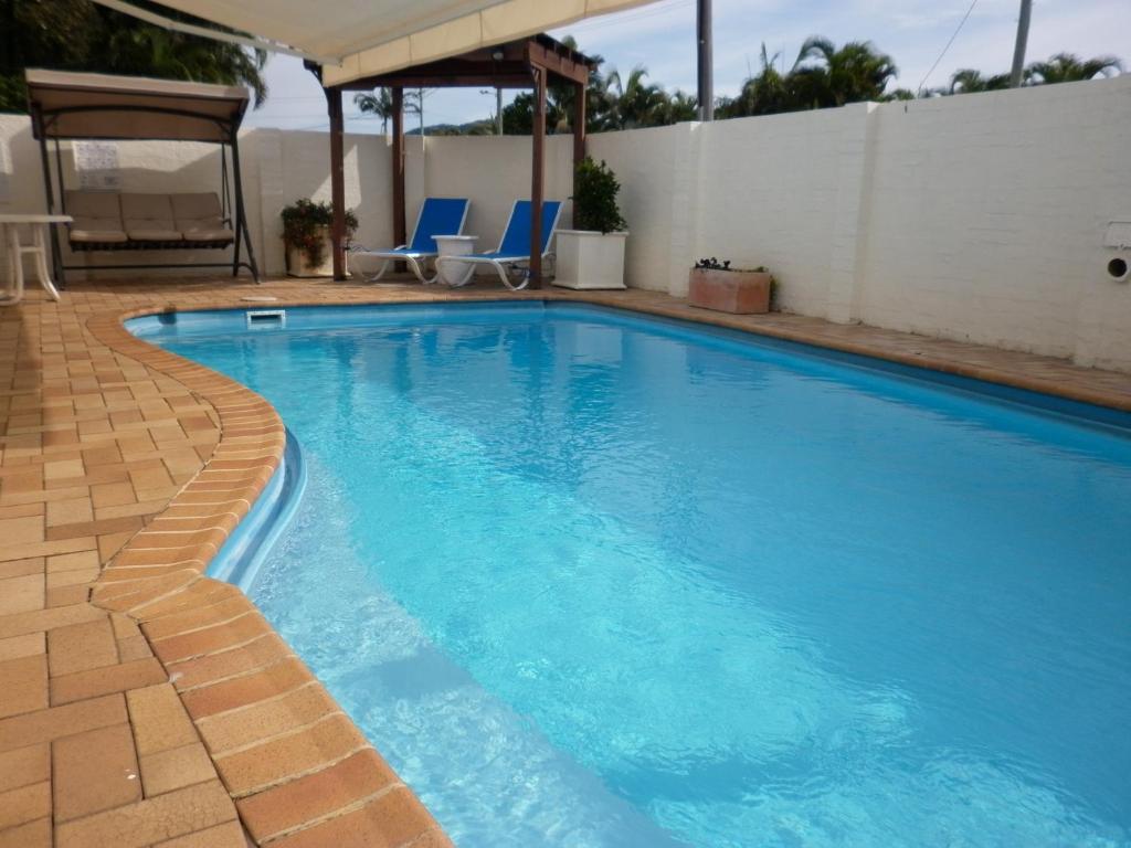 a large blue swimming pool with two blue chairs and a white wall at Oceana Holiday Units in Coffs Harbour