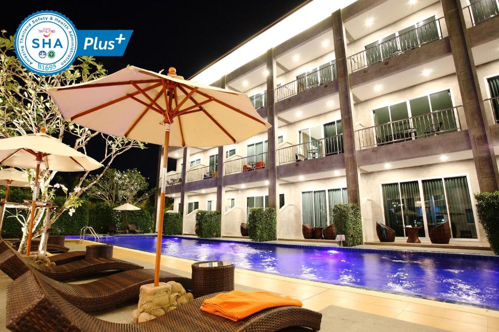 un hotel con sillas y sombrilla junto a una piscina en The Malika Hotel - SHA Extra Plus en Phuket