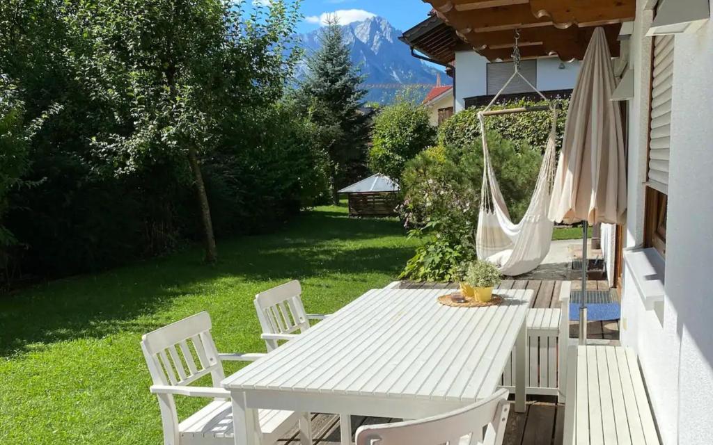 Sweet Alpen Home في غارميش - بارتنكيرشين: طاولة بيضاء وكراسي مع أرجوحة على ساحة