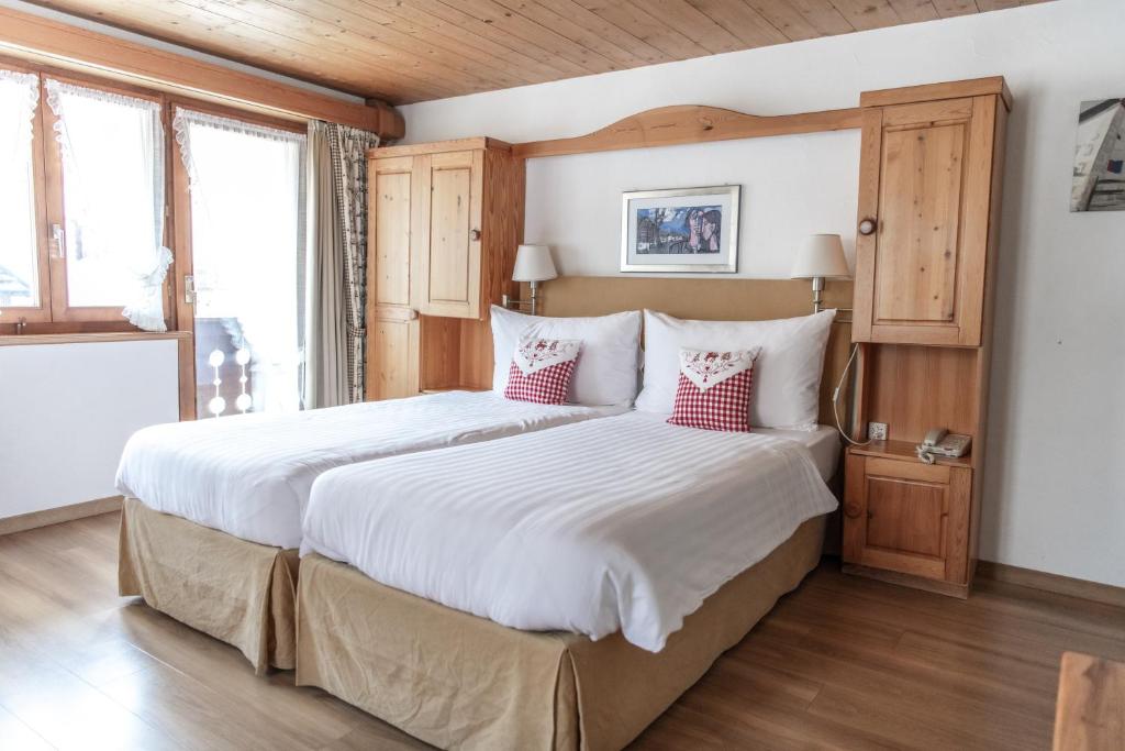 a bedroom with a large bed with white sheets and red pillows at Hotel Steinbock in Klosters