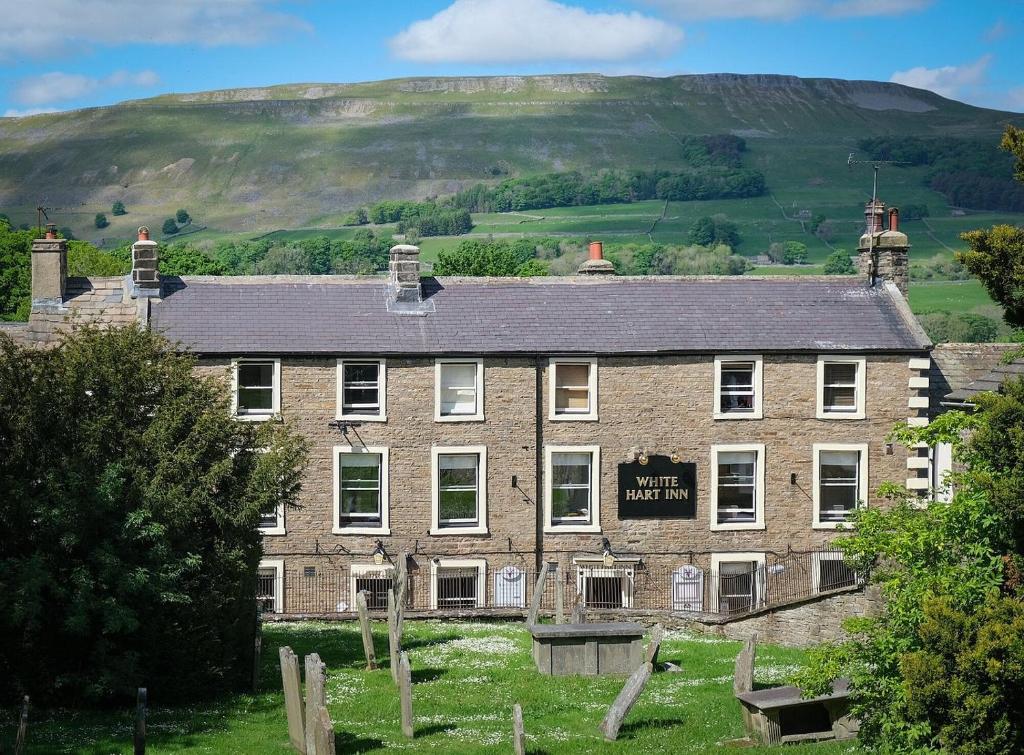 an old brick building with a hill in the background at The White Hart Inn, Hawes in Hawes