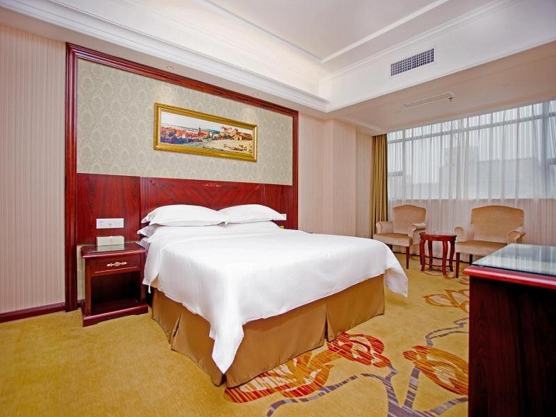 a hotel room with a large bed and a table at Vienna Hotel Shenzhen Shiyan Shilong Community in Bao'an