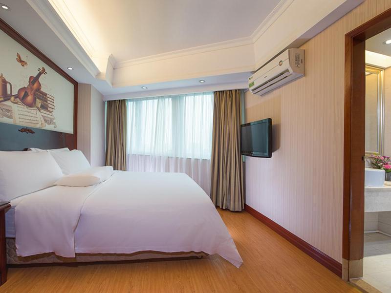 Cette chambre comprend un lit blanc et une télévision. dans l'établissement Vienna International Hotel Guangzhou Railway Station, à Canton