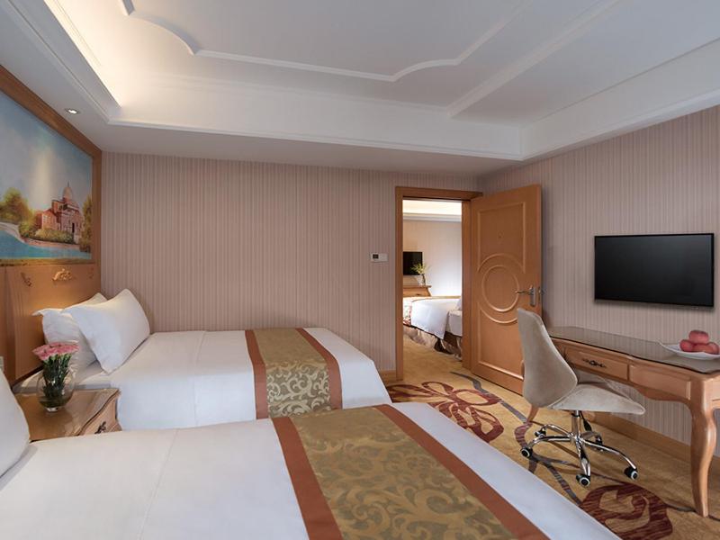 Una habitación de hotel con dos camas, un escritorio y un televisor. en Vienna International Hotel Shenzhen Jingtian, en Shenzhen