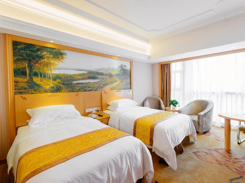 NianbalianにあるVienna International Hotel Shanghai Pudong New District Dishui Lake Univeristy Cityのベッド2台が備わる客室で、壁には絵画が飾られています。