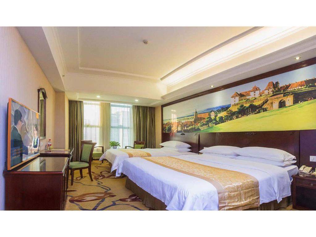 Vienna Hotel Shenzhen Fuyong Qiaotou في باوان: غرفة فندقية بسريرين ولوحة على الحائط