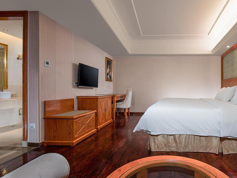 Un dormitorio con una cama y un escritorio con televisión. en Vienna Hotel Mix City, en Shenzhen