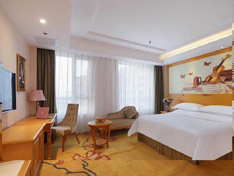 XifuにあるVienna Hotel Shandong Qingdao Chengyangの大きなベッドとデスクが備わるホテルルームです。
